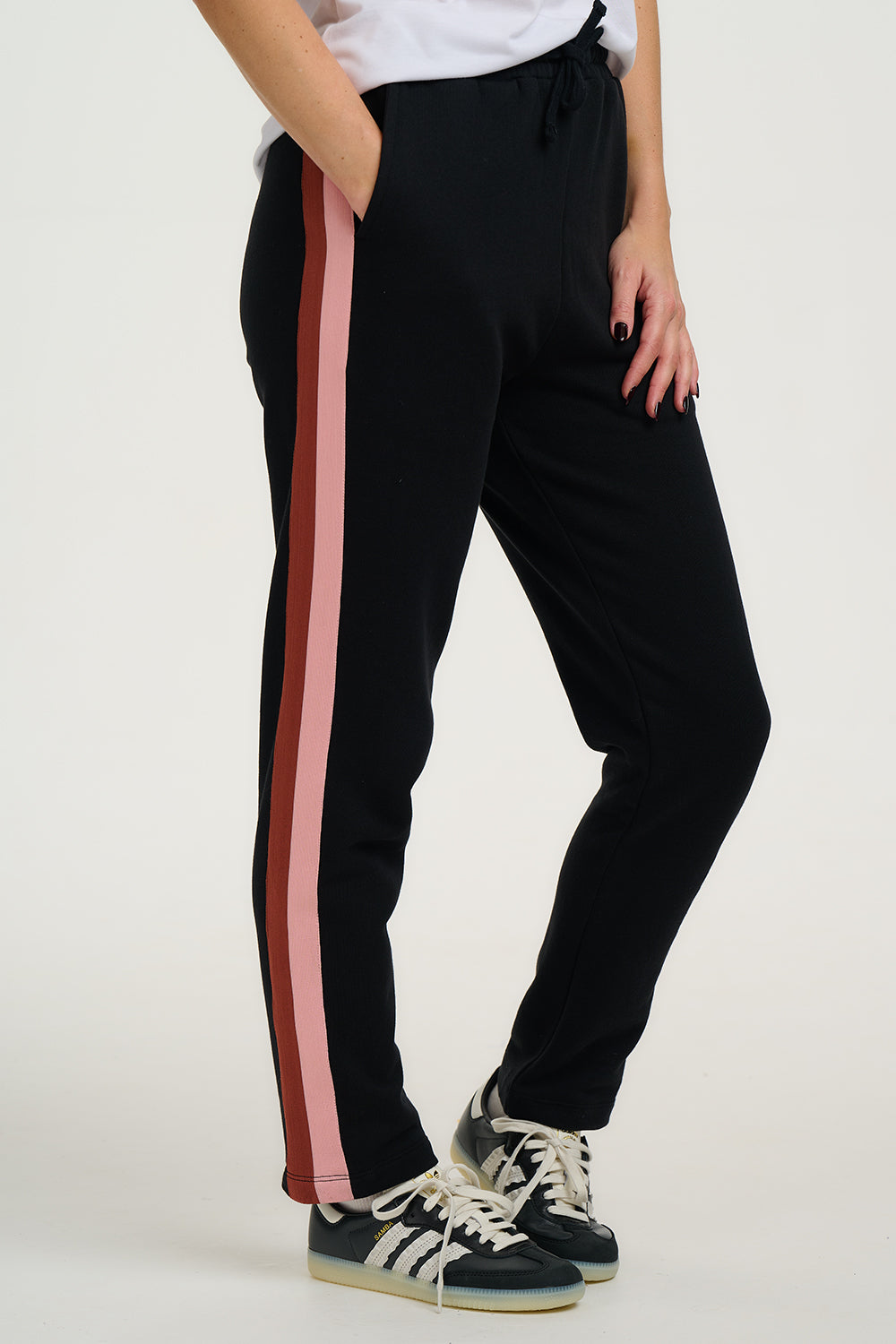 Black jogger pants with red and pink side stripes worn by a person on a white background