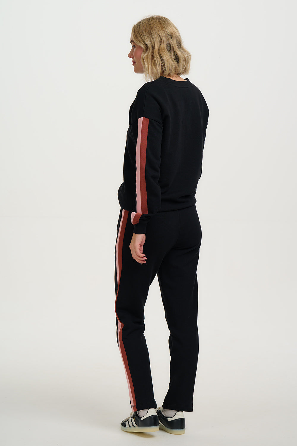 Person wearing a black tracksuit with red stripes on a white background