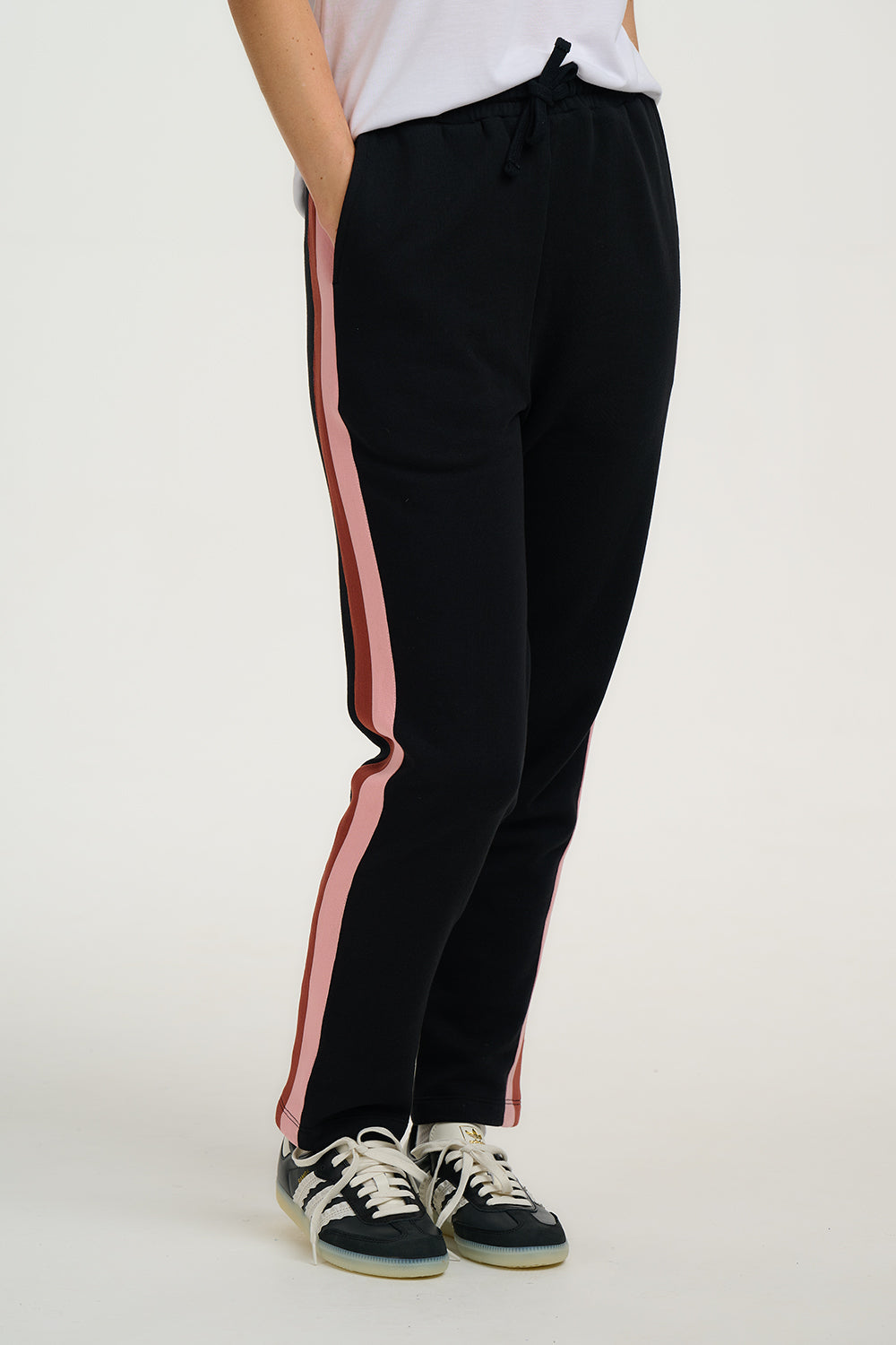 Black pants with pink side stripes worn by a person on a white background