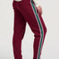 Woman wearing a cream sweater with a heart design and burgundy pants with colorful stripes on a white background
