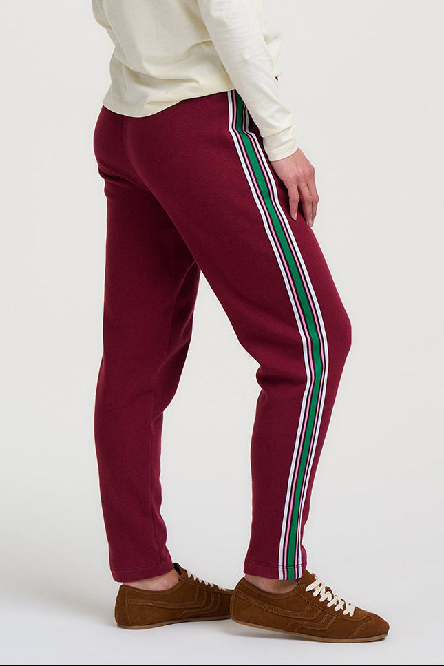 Woman wearing burgundy pants with white stripes on a white background