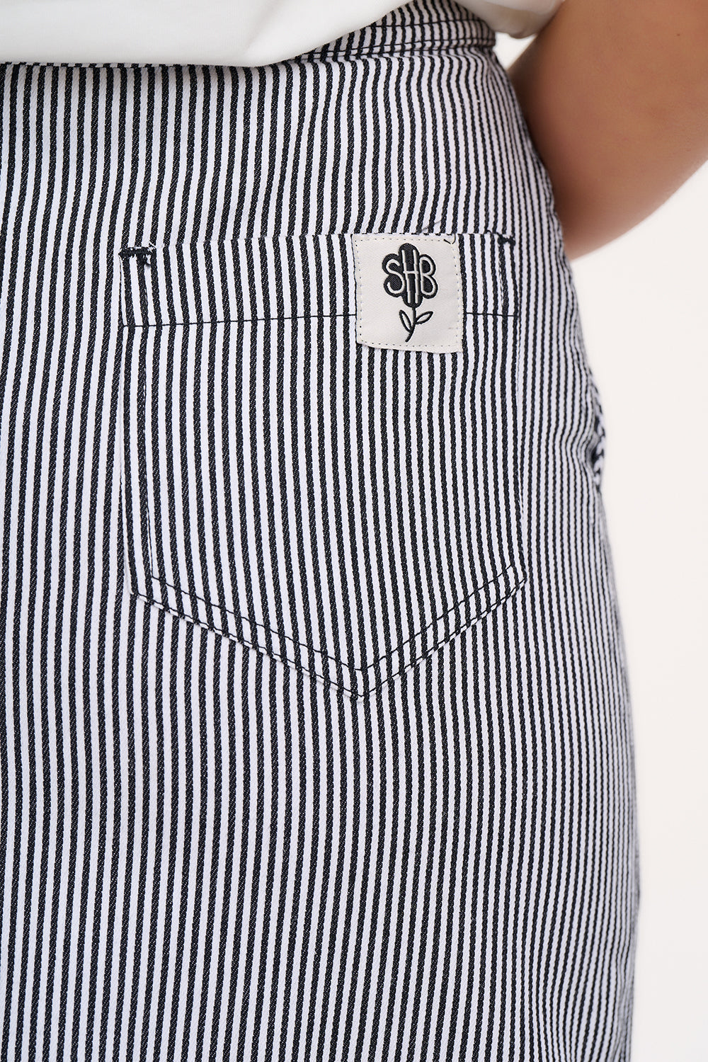 A woman wearing a fitted A-line midi skirt with monochrome stripes, paired with a white t-shirt featuring a colourful floral design, black sandals, and standing against a white background.