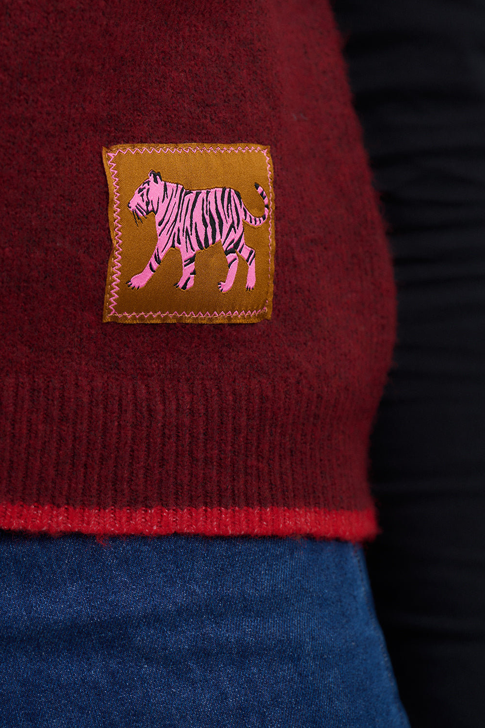 Close-up of a maroon fabric with a pink tiger patch on a dark background