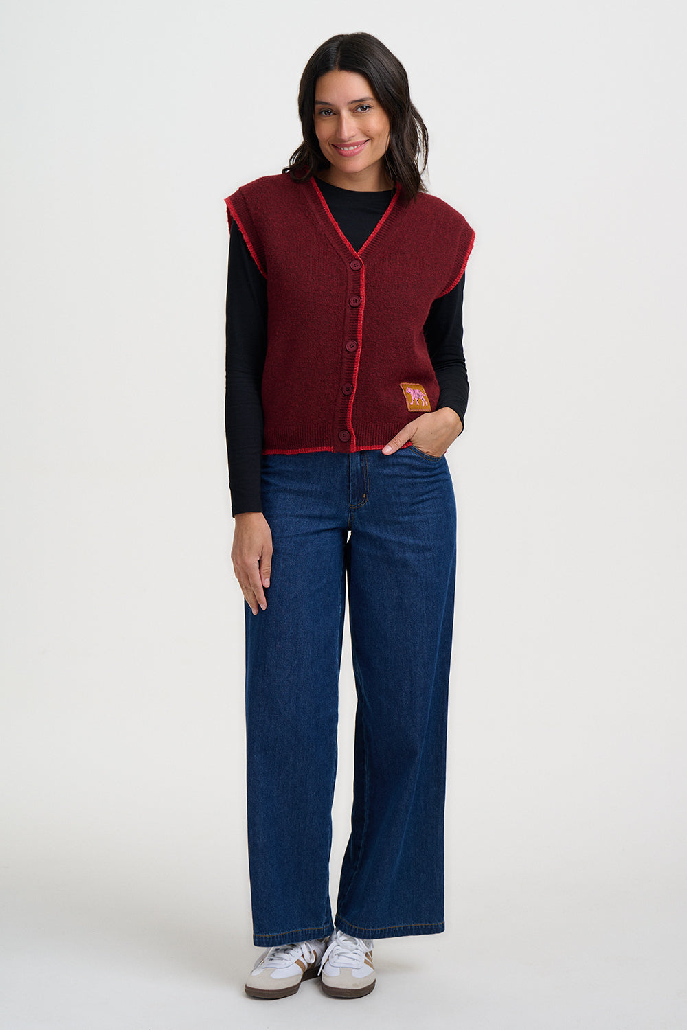 Woman wearing a red vest over a black shirt with blue jeans on a white background