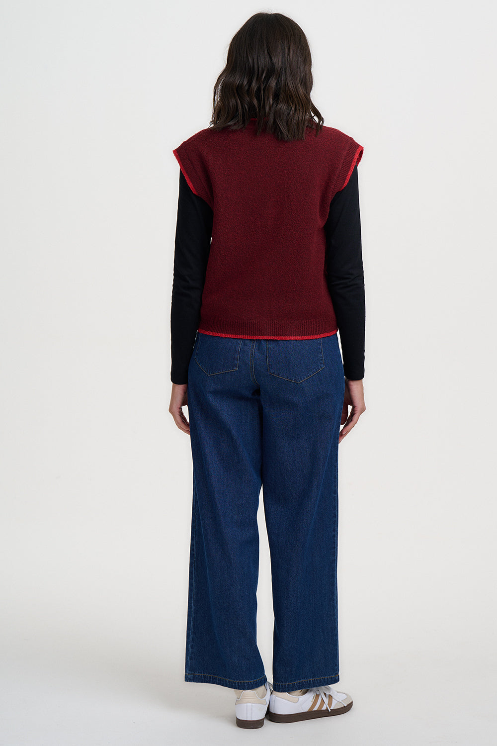 Person wearing a red sweater over a black shirt with blue jeans on a white background