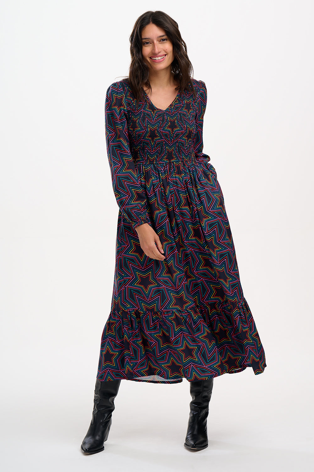 A woman wearing a midi dress with a shirred elasticated bust and long sleeves, featuring a multicolored star print on a black base.
