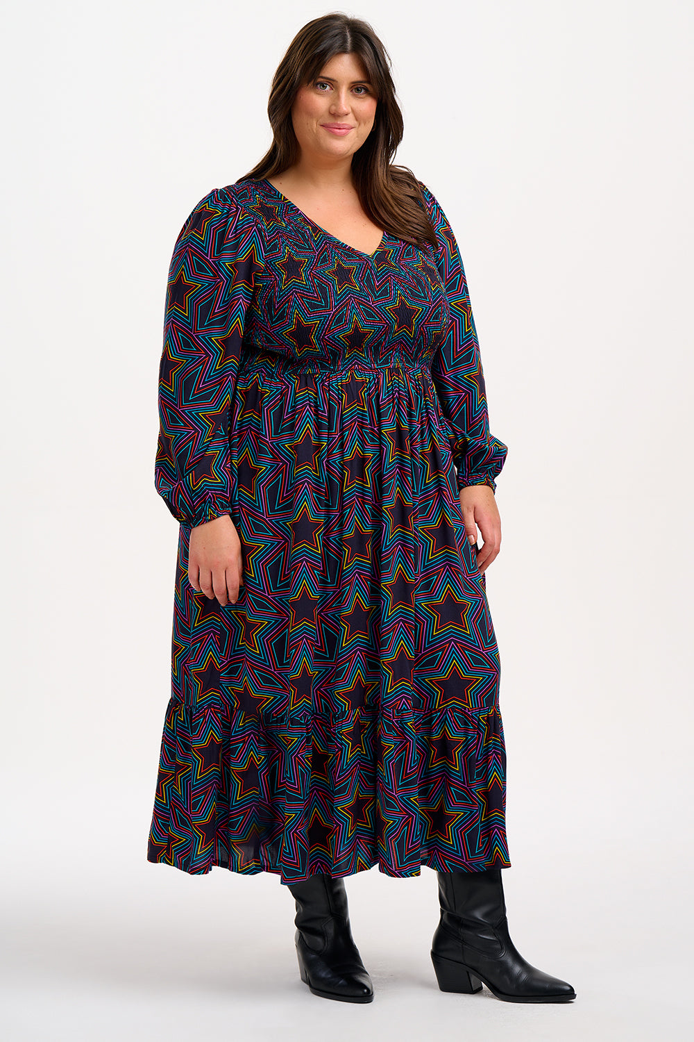 A woman wearing a midi dress with a shirred elasticated bust and long sleeves, featuring a multicolored star print on a black base.