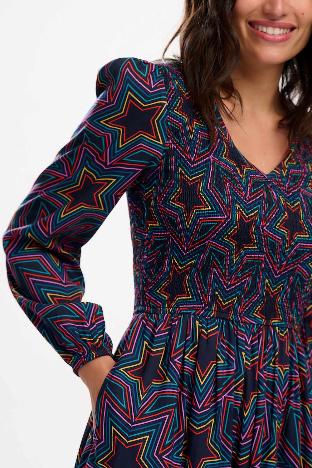 A woman wearing a midi dress with a shirred elasticated bust and long sleeves, featuring a multicolored star print on a black base.