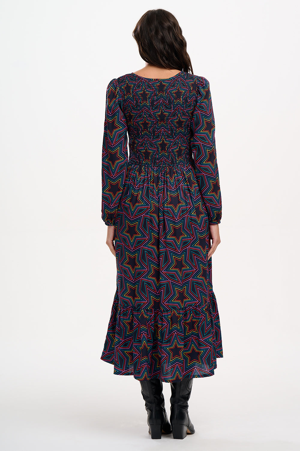 A woman wearing a midi dress with a shirred elasticated bust and long sleeves, featuring a multicolored star print on a black base.