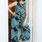 Woman wearing a patterned jumpsuit standing in a doorway.