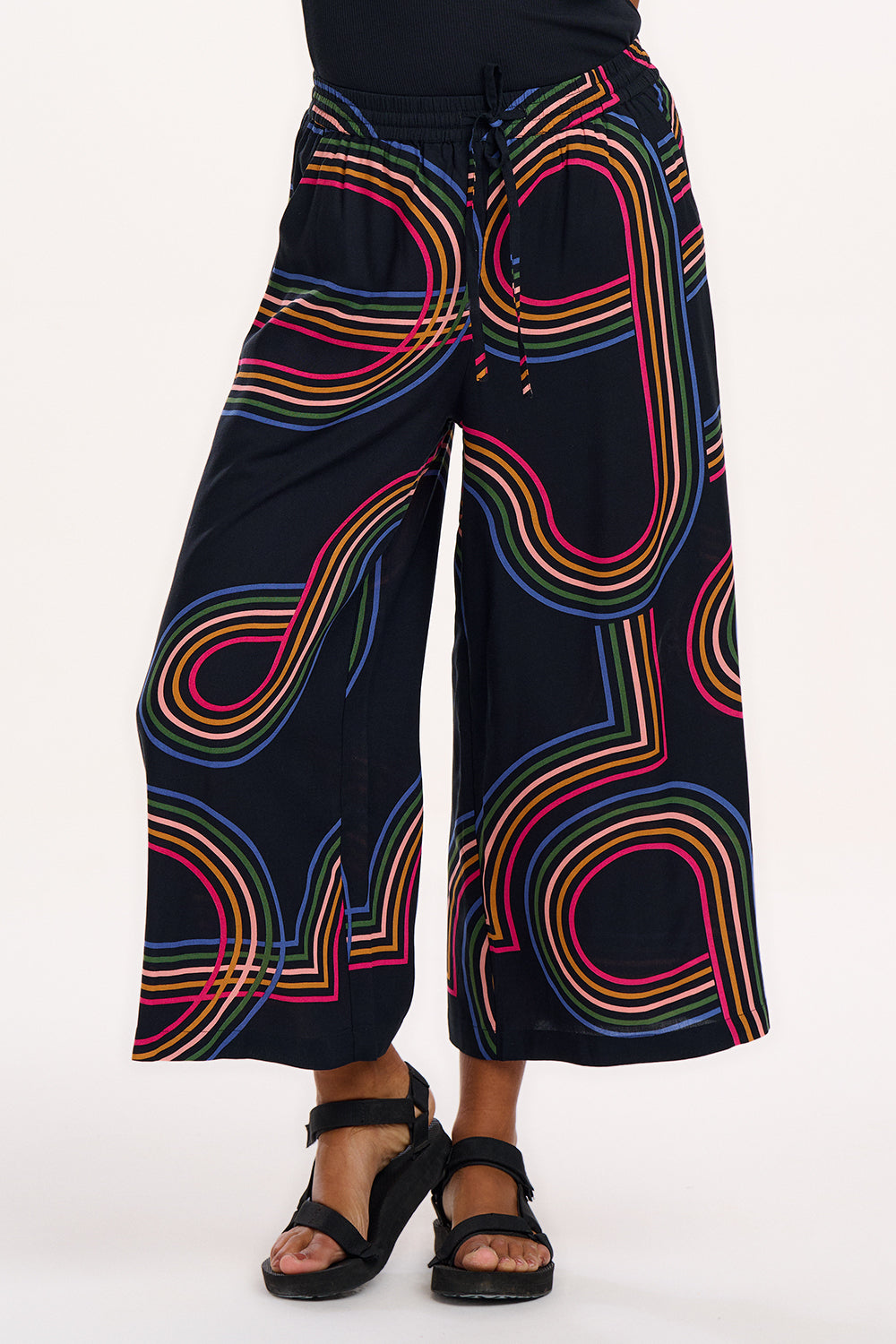 A model wearing black cropped wide-leg trousers with a geometric multicolour pattern, paired with a black tank top.