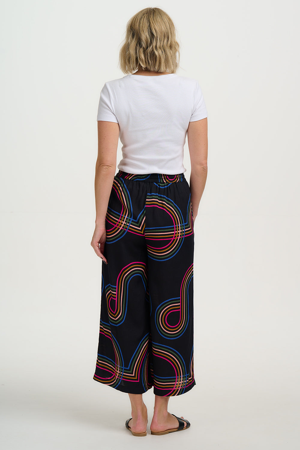 A model wearing black cropped wide-leg trousers with a geometric multicolour pattern, paired with a black tank top.