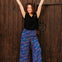 Woman in black top and colorful pants standing against a wooden door
