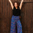 Woman in black top and colorful pants standing against a wooden door