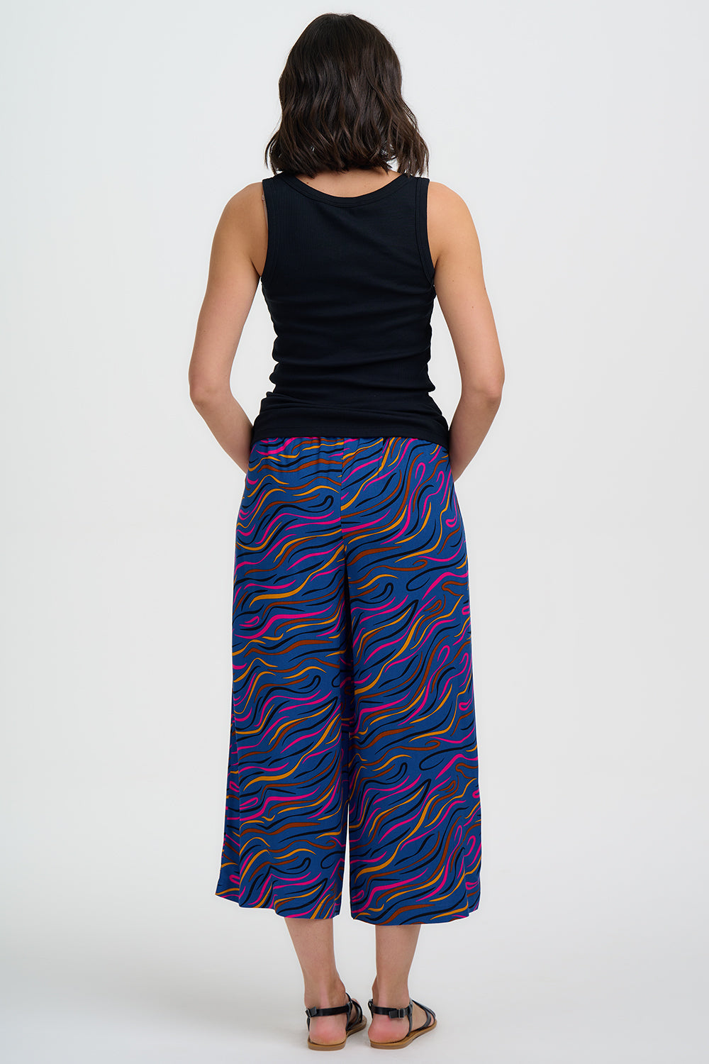 Woman wearing a black sleeveless top and colorful patterned pants on a white background