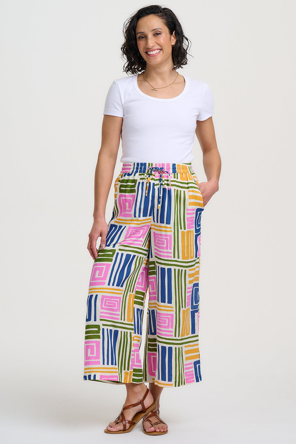 Woman wearing colorful geometric-patterned pants and a white top on a white background
