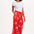 A woman modeling red cropped wide-leg trousers with a Rainbow Fronds print, paired with a white top and white sandals.