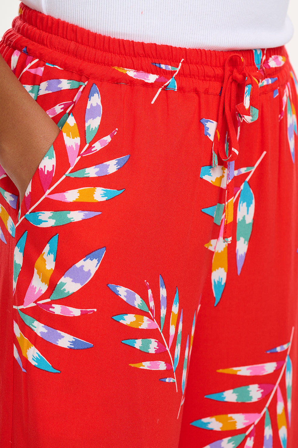 A woman modeling red cropped wide-leg trousers with a Rainbow Fronds print, paired with a white top and white sandals.