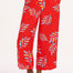 A model wearing red cropped wide-leg trousers with a colorful leaf pattern, standing against a white background.