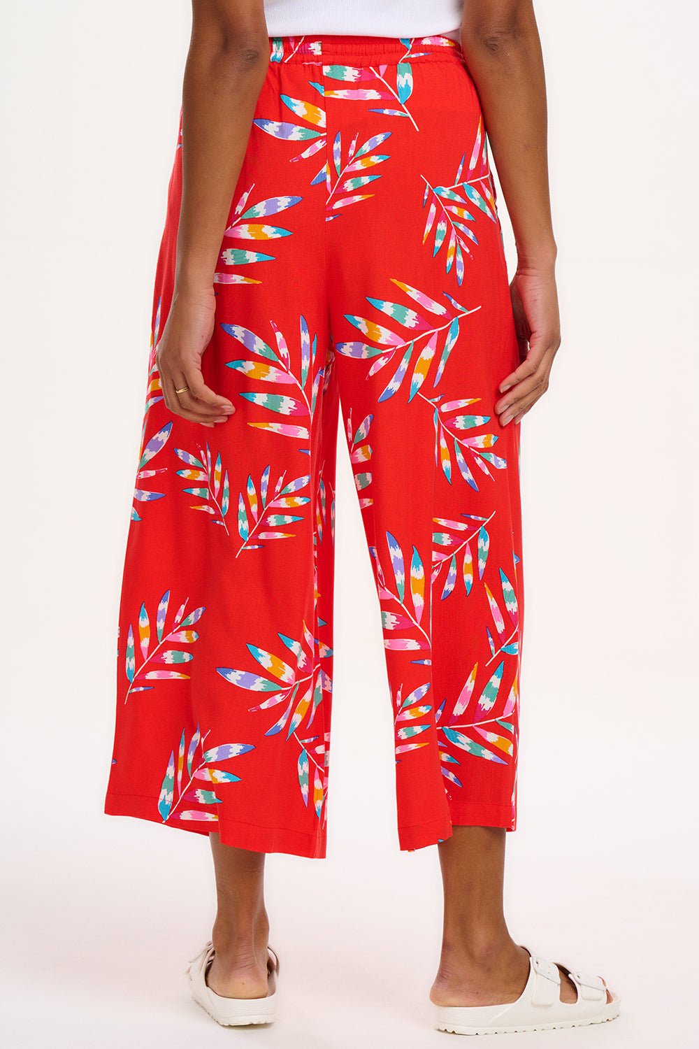 A woman modeling red cropped wide-leg trousers with a Rainbow Fronds print, paired with a white top and white sandals.