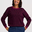 A woman wearing a long-sleeve crewneck sweater with a dark purple and black wavy stripe pattern, paired with blue jeans, against a light gray studio background.