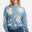 A woman wearing a blue and cream colored intarsia knit jumper with a tropical nights design, including white parrots, palm trees, stars, and suns on a pastel blue base.