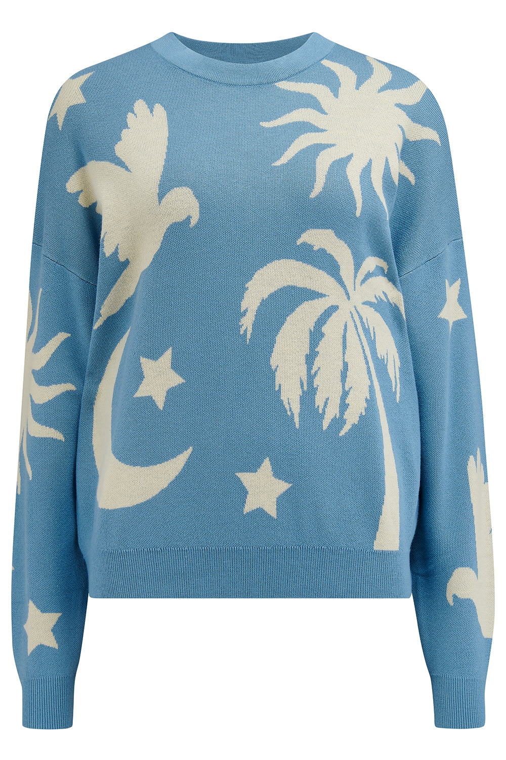 A woman wearing a blue and cream colored intarsia knit jumper with a tropical nights design, including white parrots, palm trees, stars, and suns on a pastel blue base.