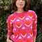 Person wearing a pink sweater with red heart patterns against a natural background