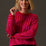Woman wearing a bright pink sweater with wavy pattern against a plain background