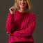 Woman wearing a bright pink sweater with wavy pattern against a plain background