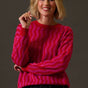 Woman wearing a bright pink sweater with wavy pattern against a plain background