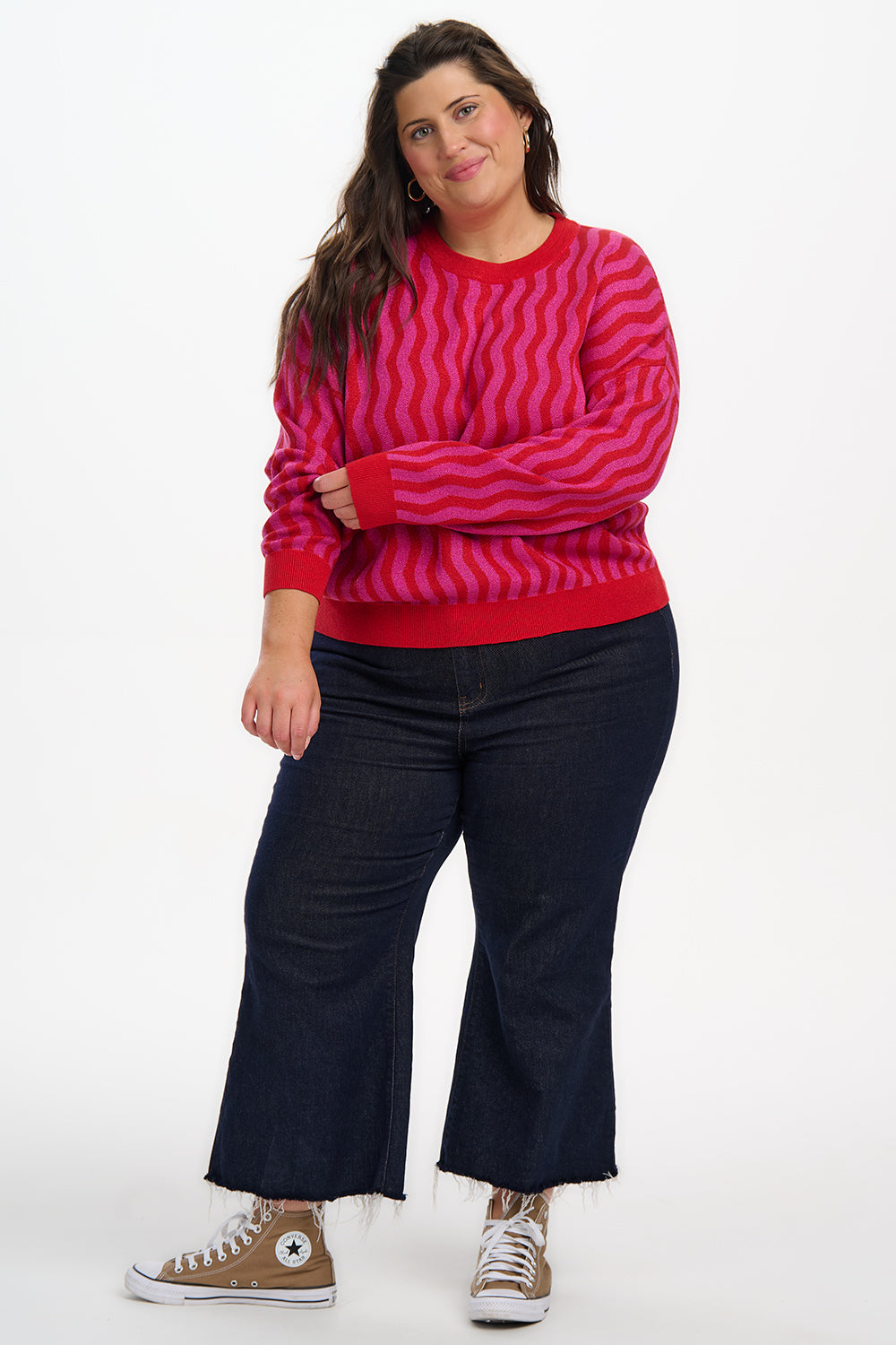 Person wearing a red and pink striped sweater with dark pants and brown shoes on a white background