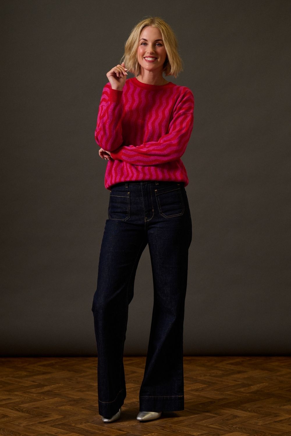 Woman wearing a bright pink sweater and dark jeans against a plain background