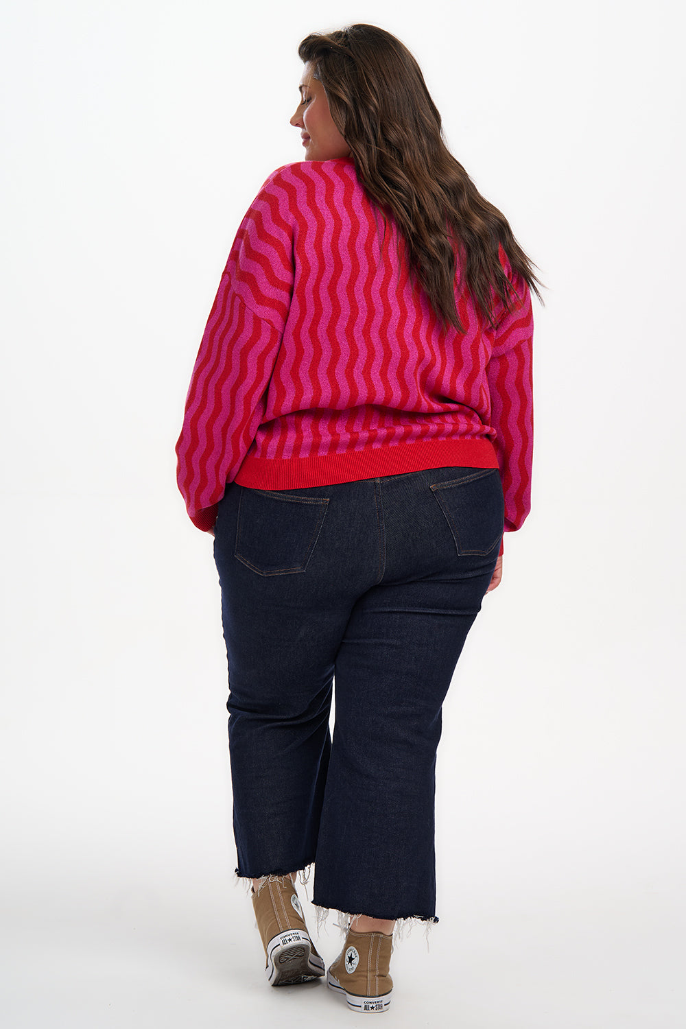 Person wearing a red and pink patterned sweater and dark blue jeans on a white background