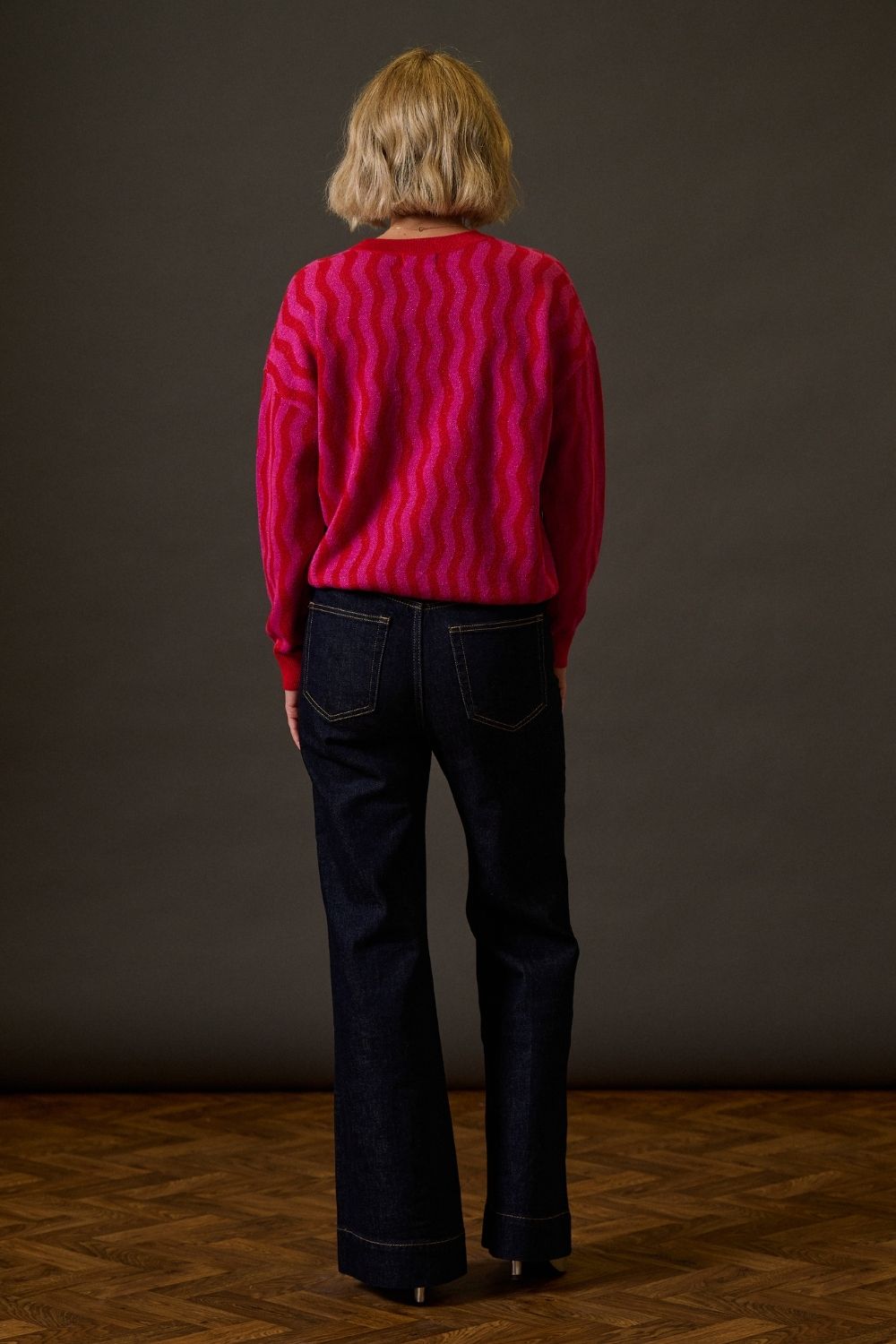 Person wearing a red sweater and dark jeans standing against a plain background