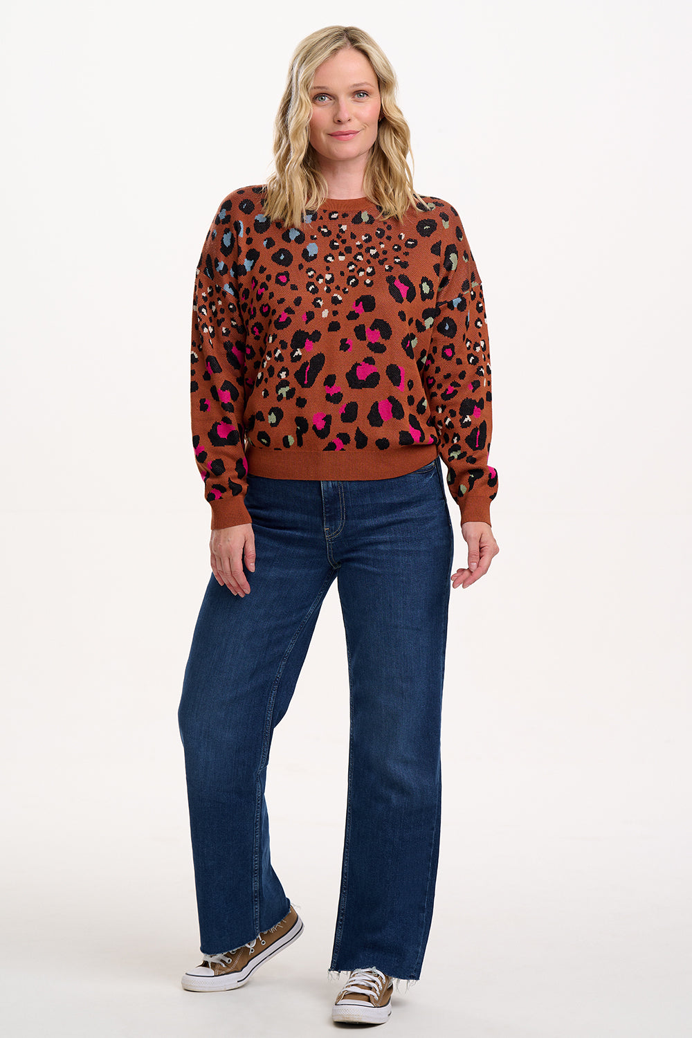 Woman wearing a brown sweater with colorful animal print and blue jeans on a white background