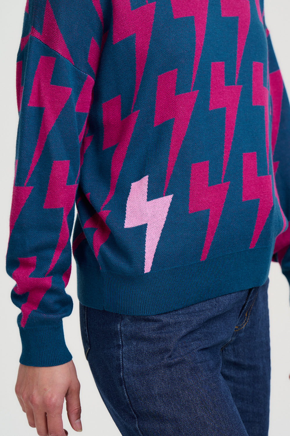 Blue sweater with pink lightning bolt pattern worn by a person on a white background