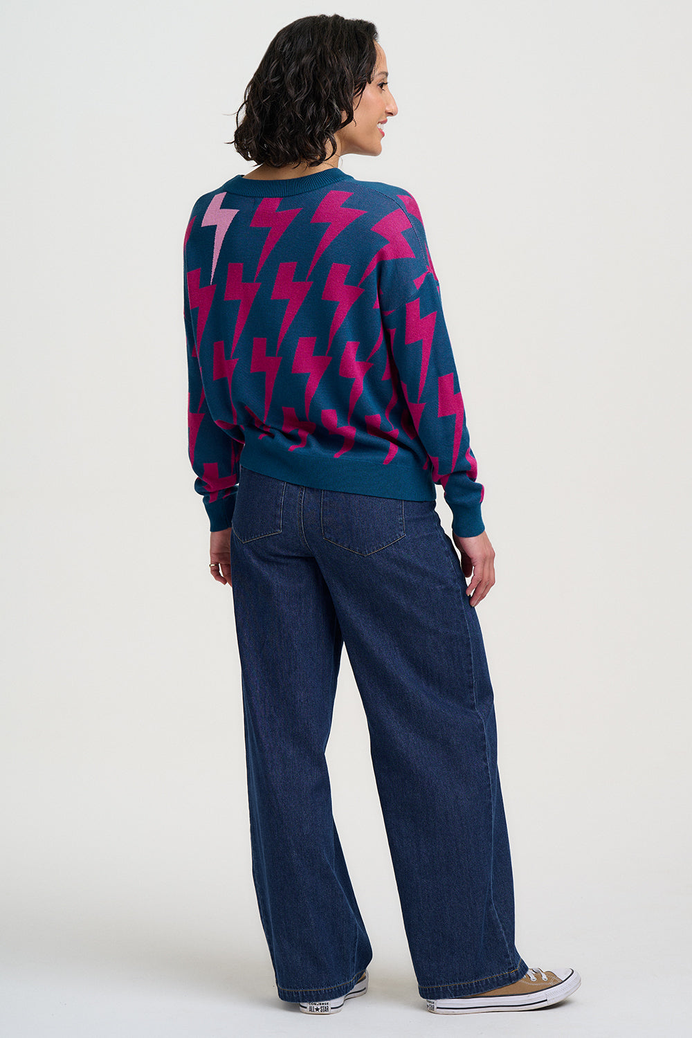 Person wearing a blue sweater with pink lightning bolt patterns and blue jeans on a white background