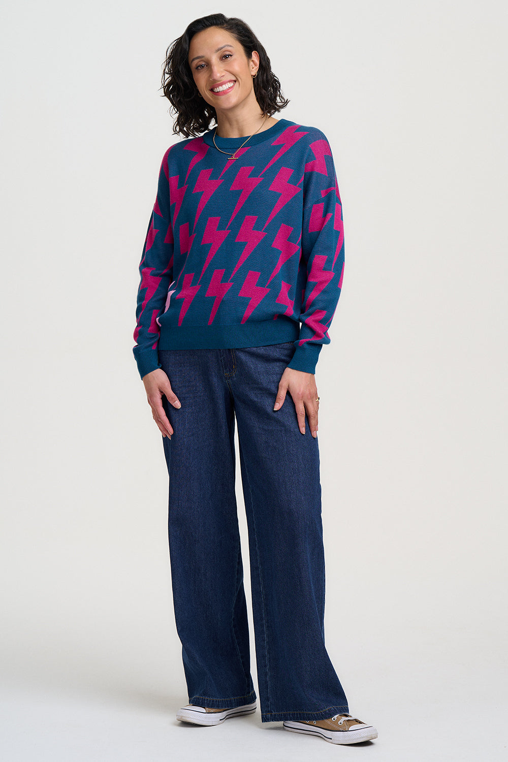 Woman wearing a blue sweater with pink lightning bolt patterns and blue jeans on a white background