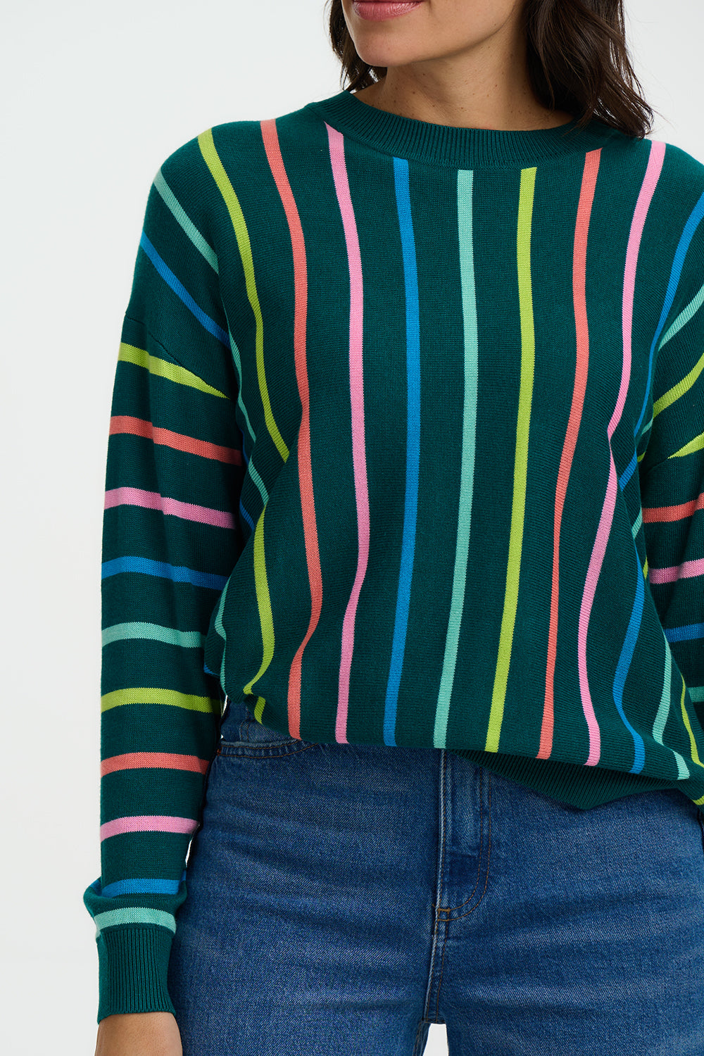 Person wearing a green sweater with colorful vertical stripes and blue jeans.