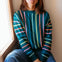 Woman wearing a colorful striped sweater sitting by a window.