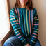 Woman wearing a colorful striped sweater sitting by a window.