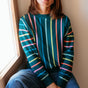 Woman wearing a colorful striped sweater sitting by a window.