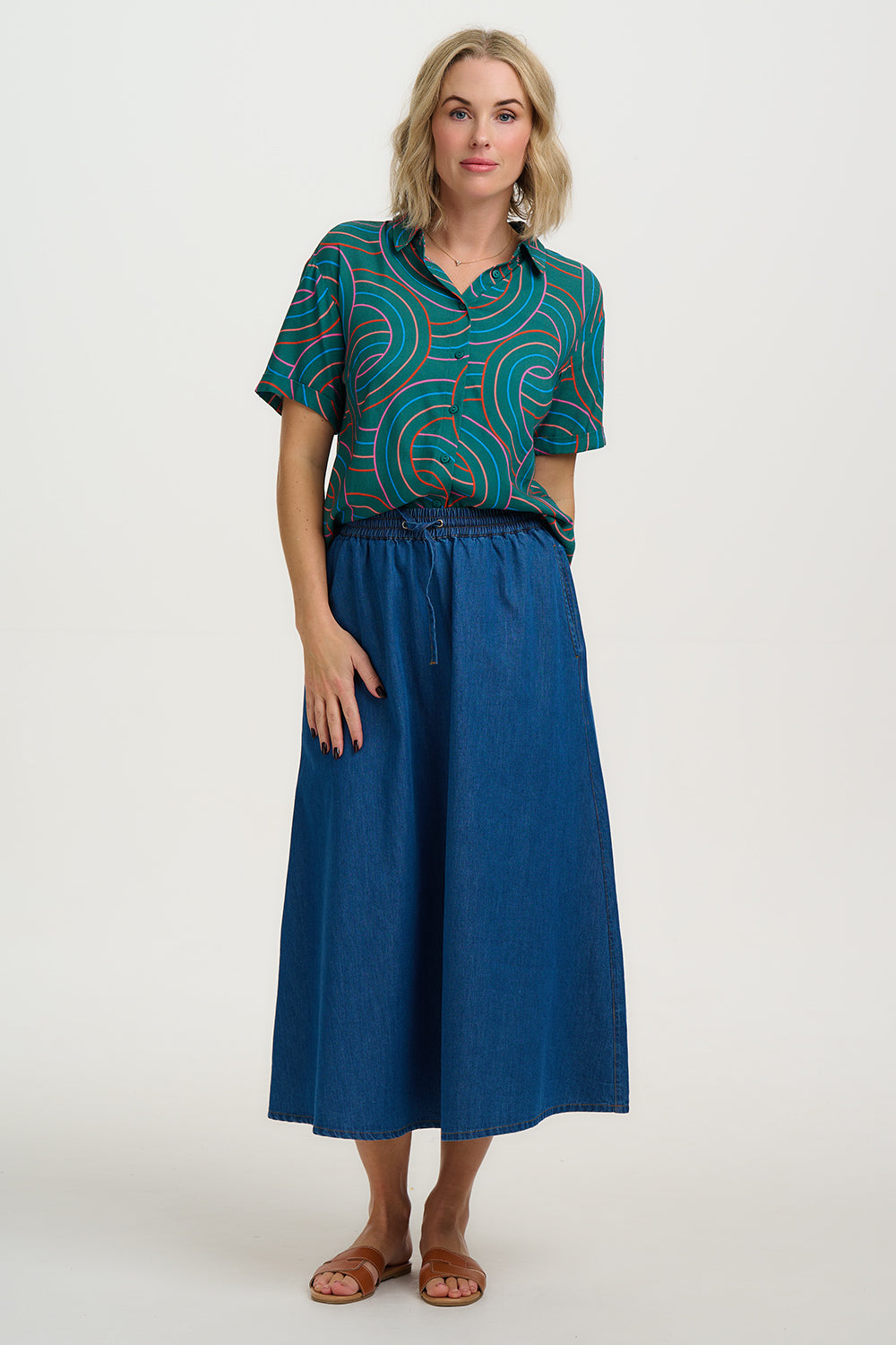 Woman wearing a patterned top and blue skirt on a white background
