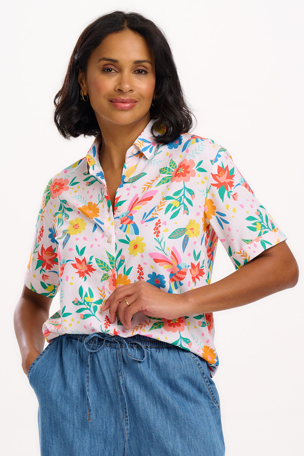 A woman wearing an off-white shirt with a tropical hummingbird print, short sleeves, and rolled-up cuffs.