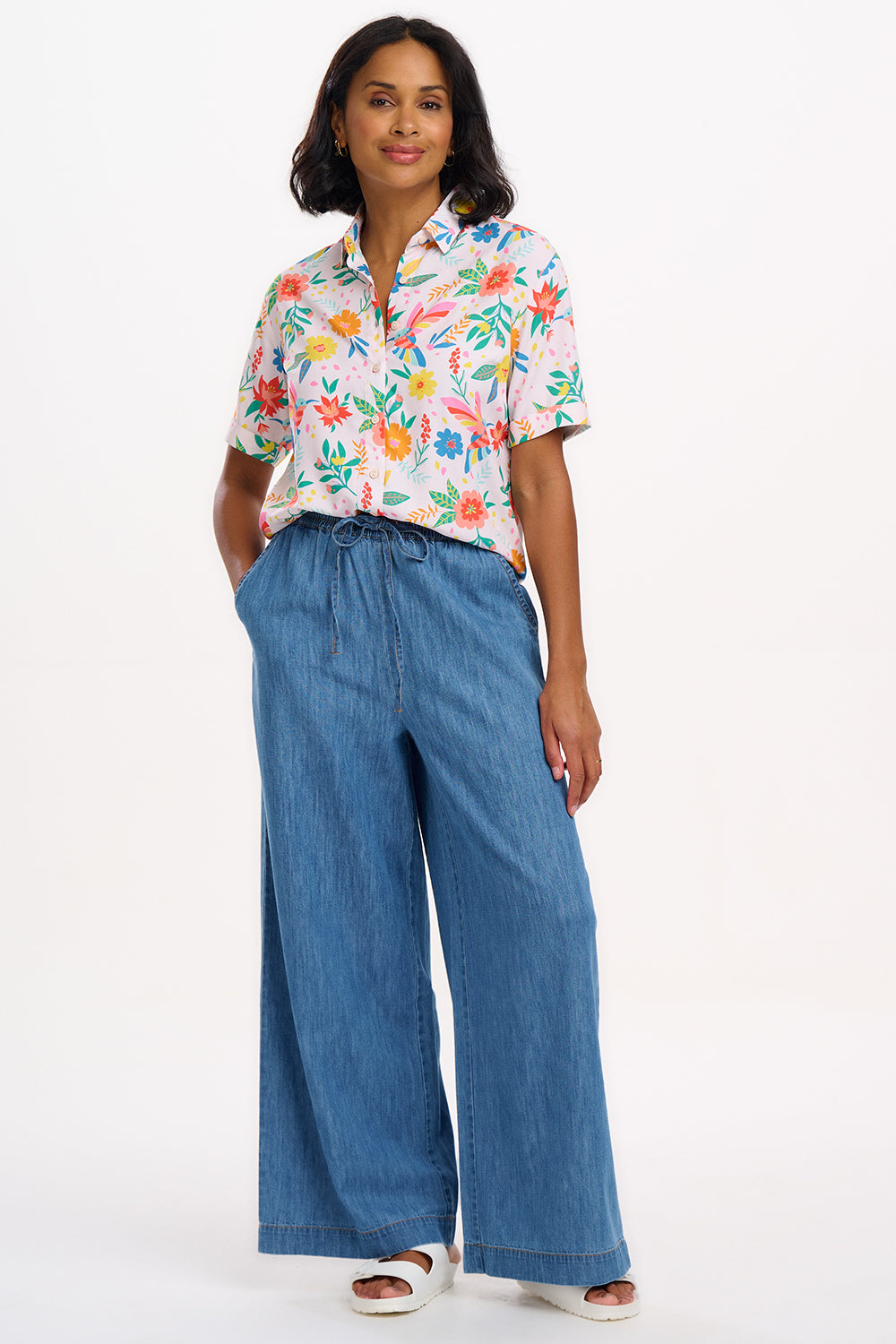 A woman wearing an off-white shirt with a tropical hummingbird print, short sleeves, and rolled-up cuffs.