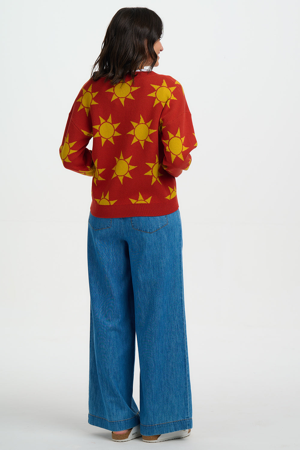 Person wearing a red sweater with yellow sun patterns and blue jeans on a white background