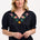 A woman wearing a black Angelique blouse with floral embroidery, short frill sleeves, and a V-neckline.