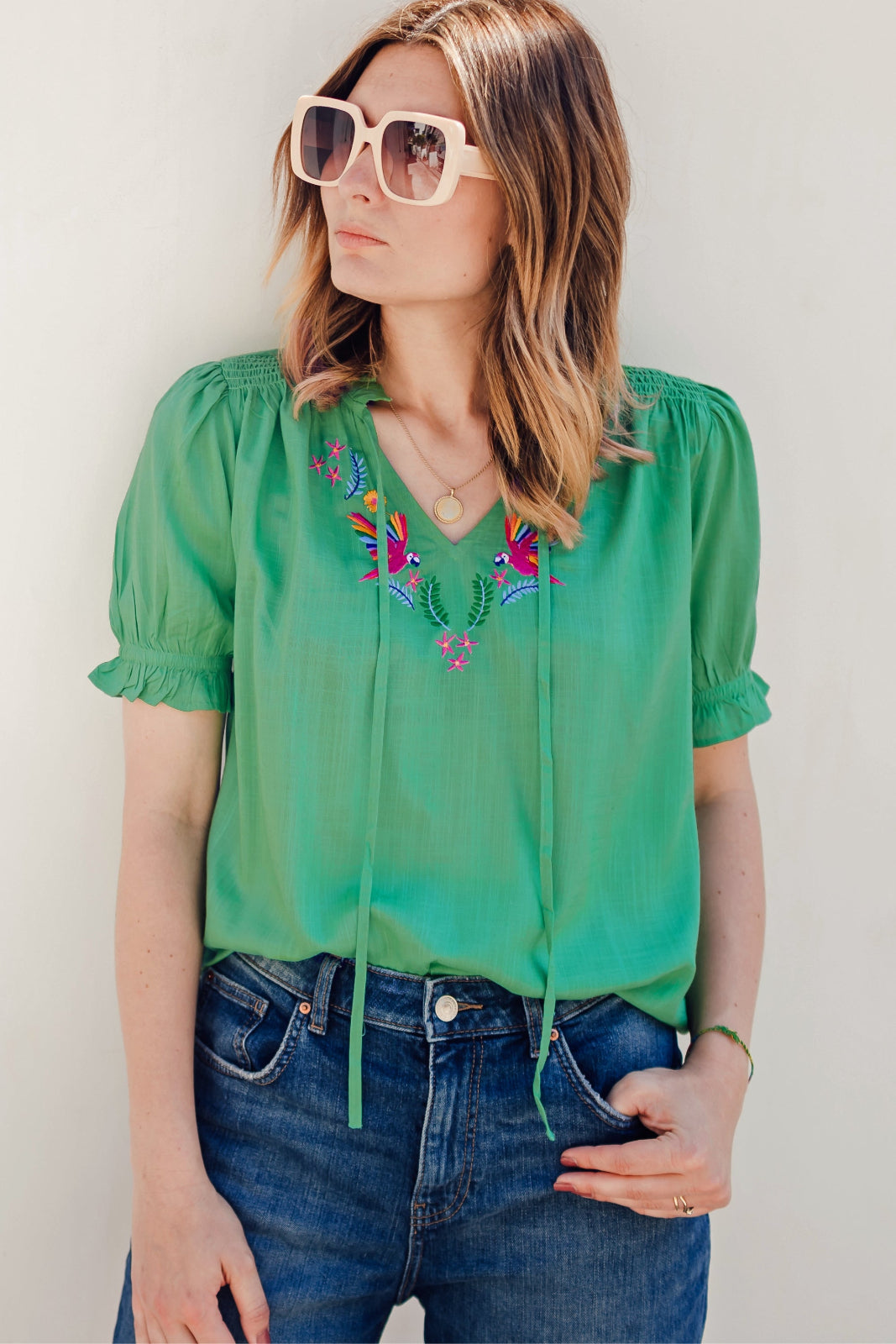 A woman wearing a green blouse with short blouson sleeves, a frill collar, and colorful parrot embroidery