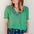 A woman wearing a green blouse with short blouson sleeves, a frill collar, and colorful parrot embroidery